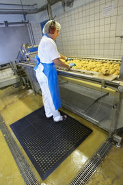 Dark anti-fatigue mat with dot grid surface beneath industrial worker