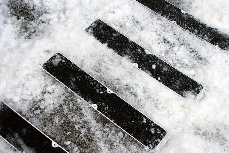 Set of black aluminum stair tread plates with non-slip grooves in snow, bolt holes