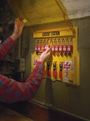 Lockout station mounted on wall with person reaching to secure padlocks