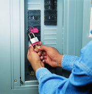 Breaker lockout mounted in electrical panel with padlock locked by hand
