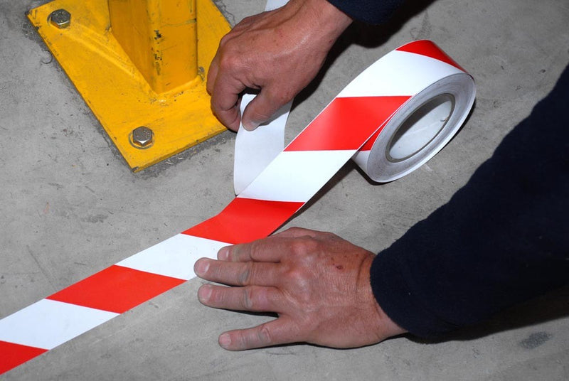 Floor hazard tape roll and striped tape in red and white, being applied by hands